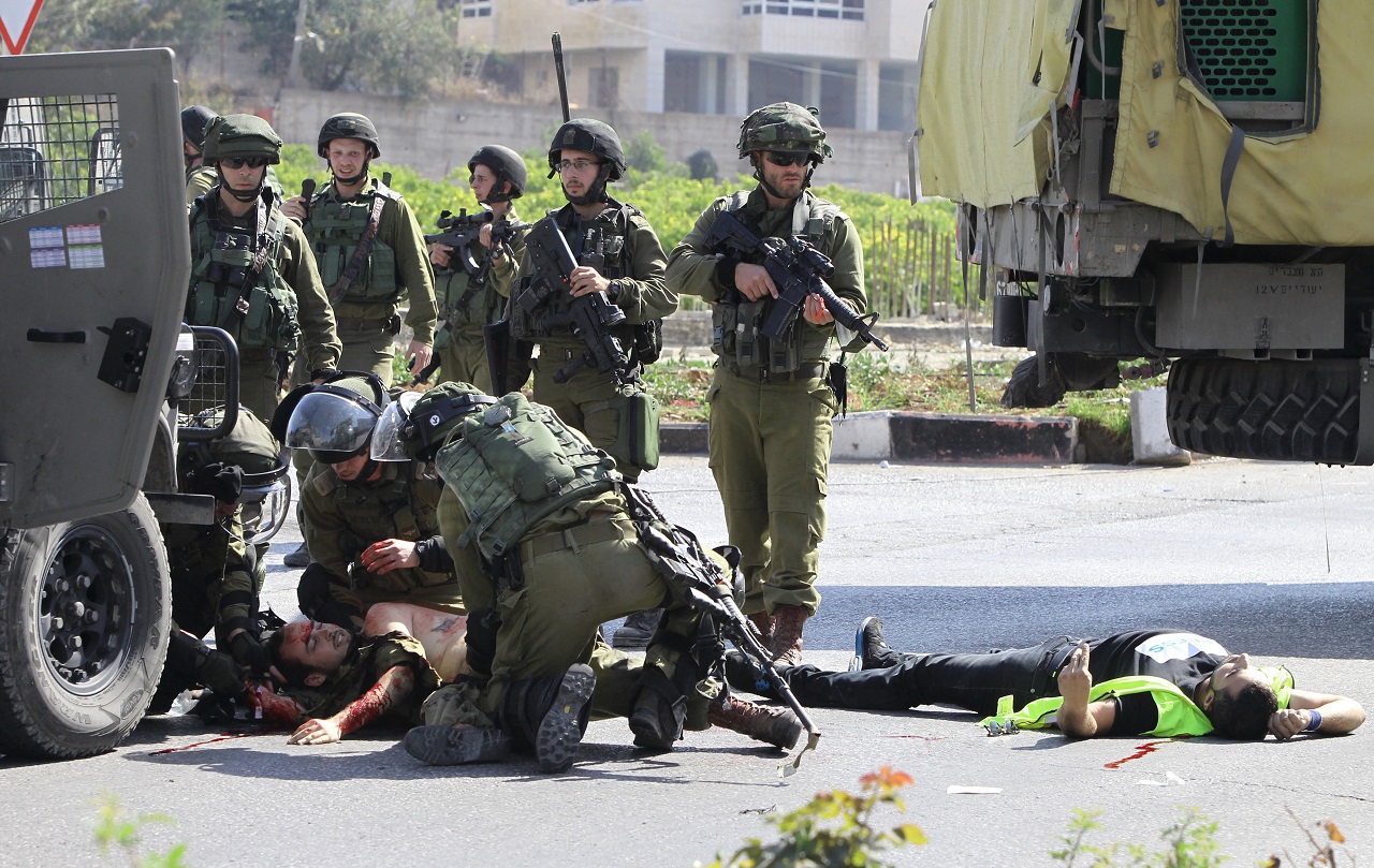 Sérült izraeli katonát ápolnak a társai, miután egy palesztin merénylő megkéselte. A merénylőt lelőtték. (AFP)