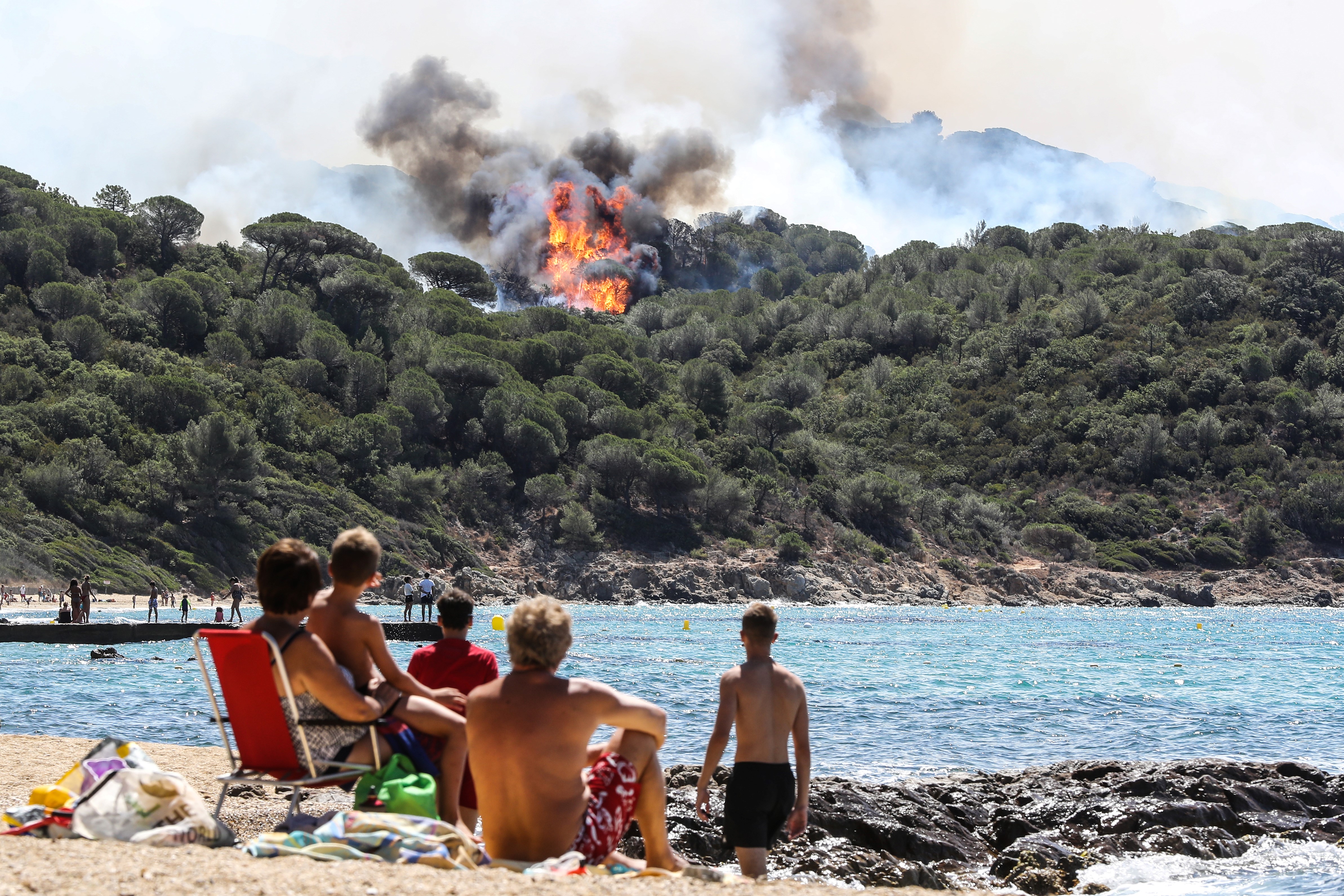 People enjoy the beach as they look at a forest fire in La Croix-Valmer, near Saint-Tropez, on July 25, 2017..Firefighters battle blazes that have consumed swathes of land in southeastern France for a second day, with one inferno out of control near the chic resort of Saint-Tropez, emergency services say.