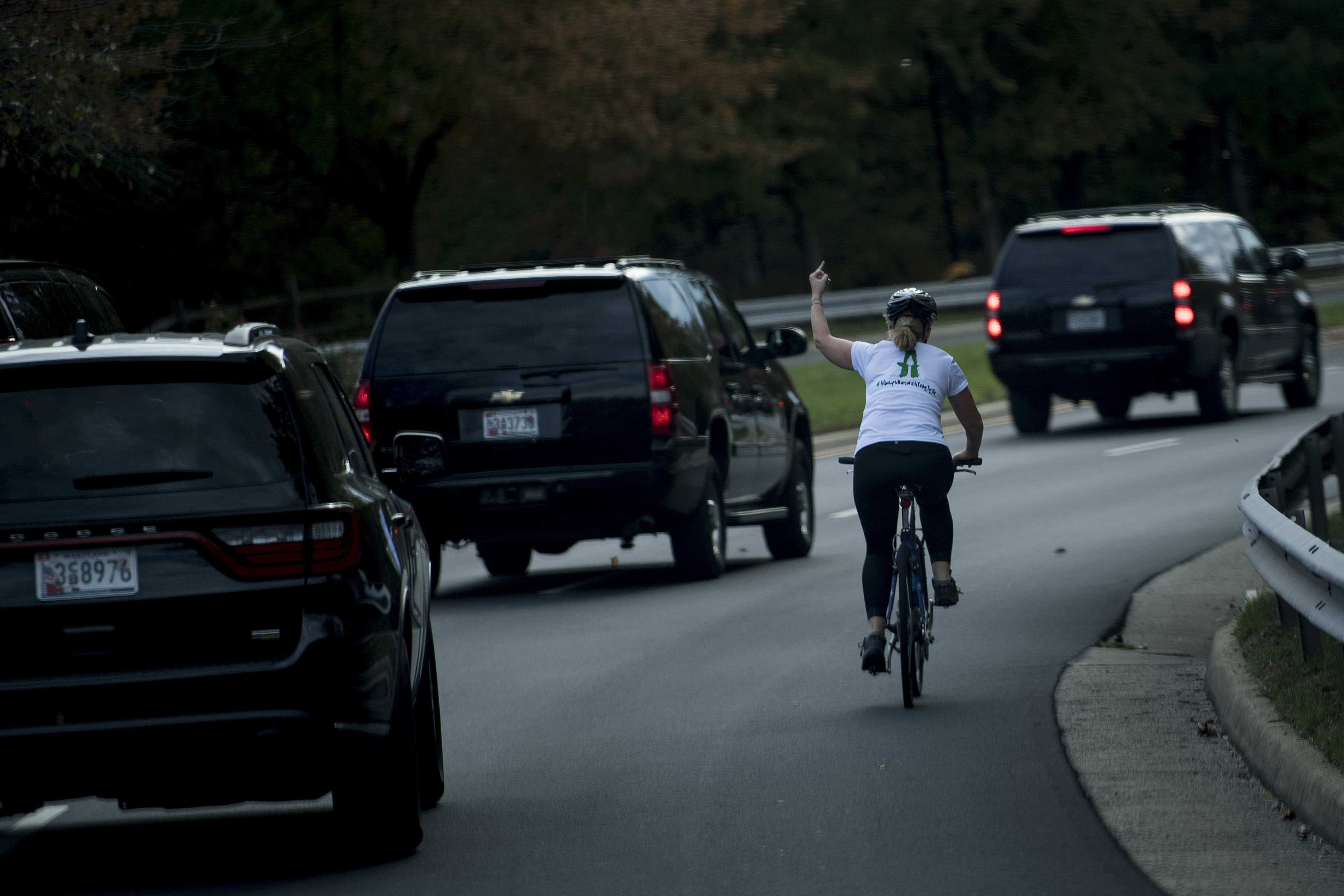 A woman on a bike gestures with her middle finger as a motorcade with US President Donald Trump departs Trump National Golf Course October 28, 2017 in Sterling, Virginia