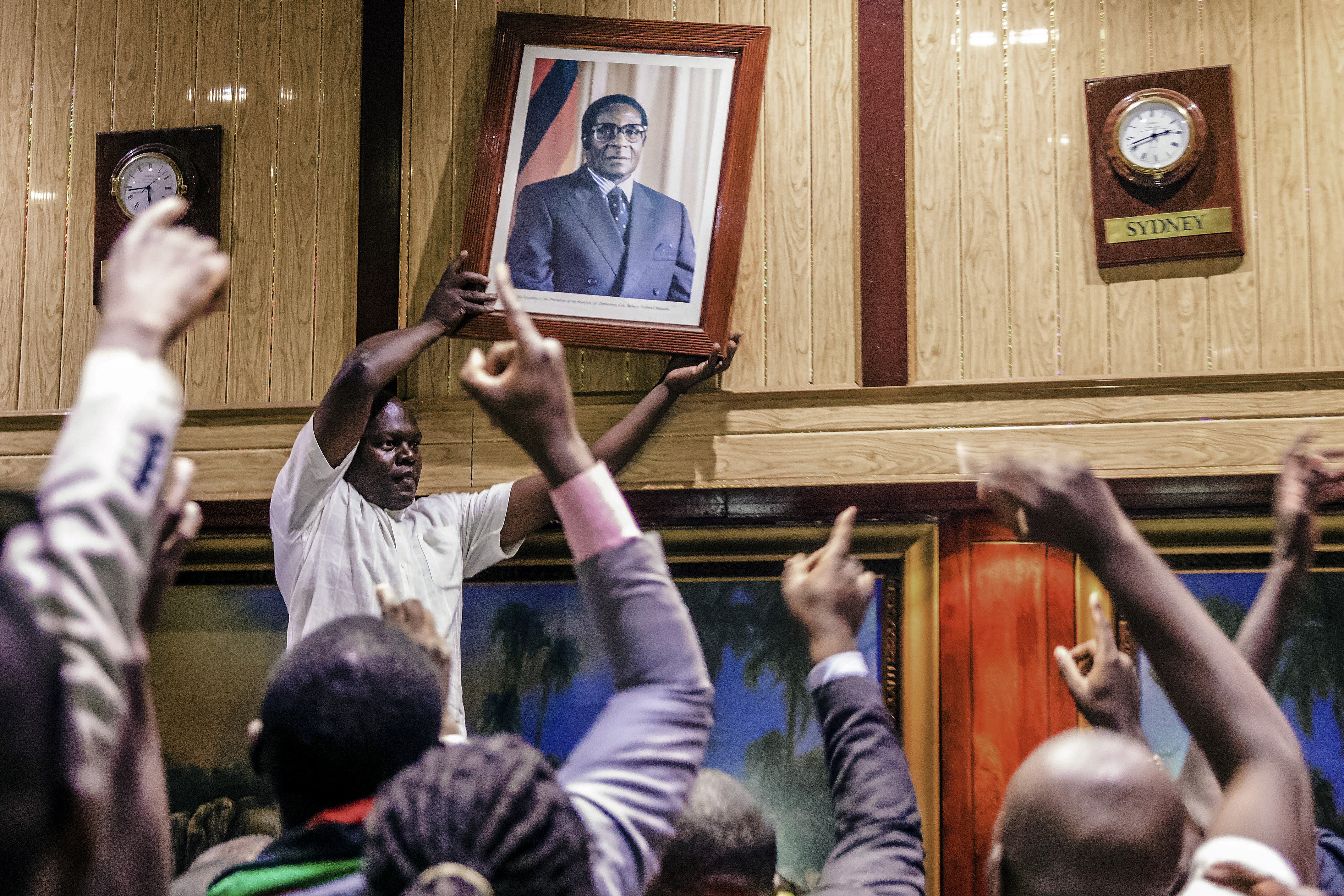 People remove, from the wall at the International Conference centre, where parliament had their sitting, the portrait of former Zimbabwean President Robert Mugabe after his resignation on November 21, 2017 in Harare..Robert Mugabe resigned as president of Zimbabwe on November 21, 2017 swept from power as his 37-year reign of brutality and