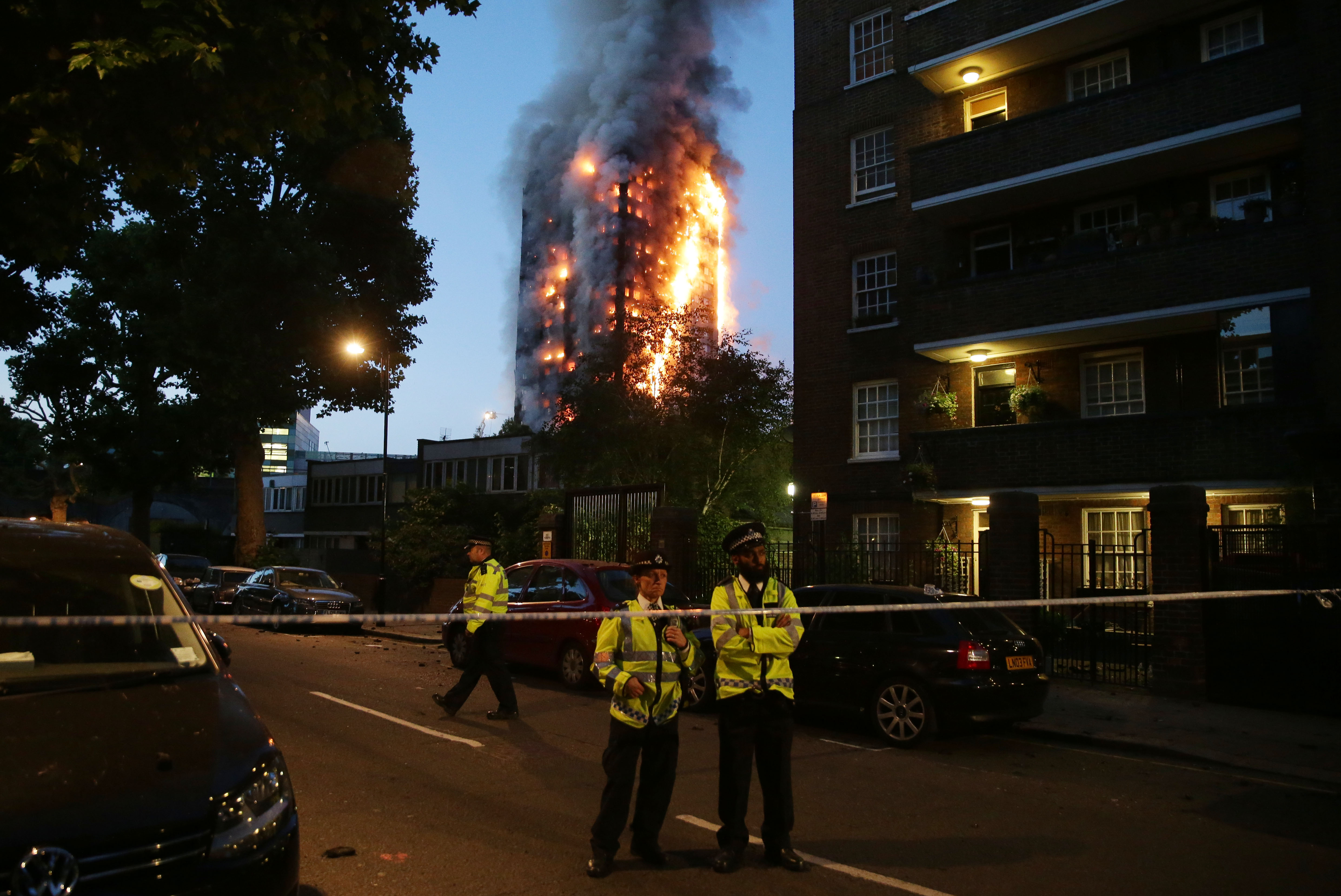Police man a security cordon as a huge fire engulfs the Grenfell Tower early June 14, 2017 in west London. .The massive fire ripped through the 27-storey apartment block in west London in the early hours of Wednesday, trapping residents inside as 200 firefighters battled the blaze. Police and fire services attempted to evacuate the concrete