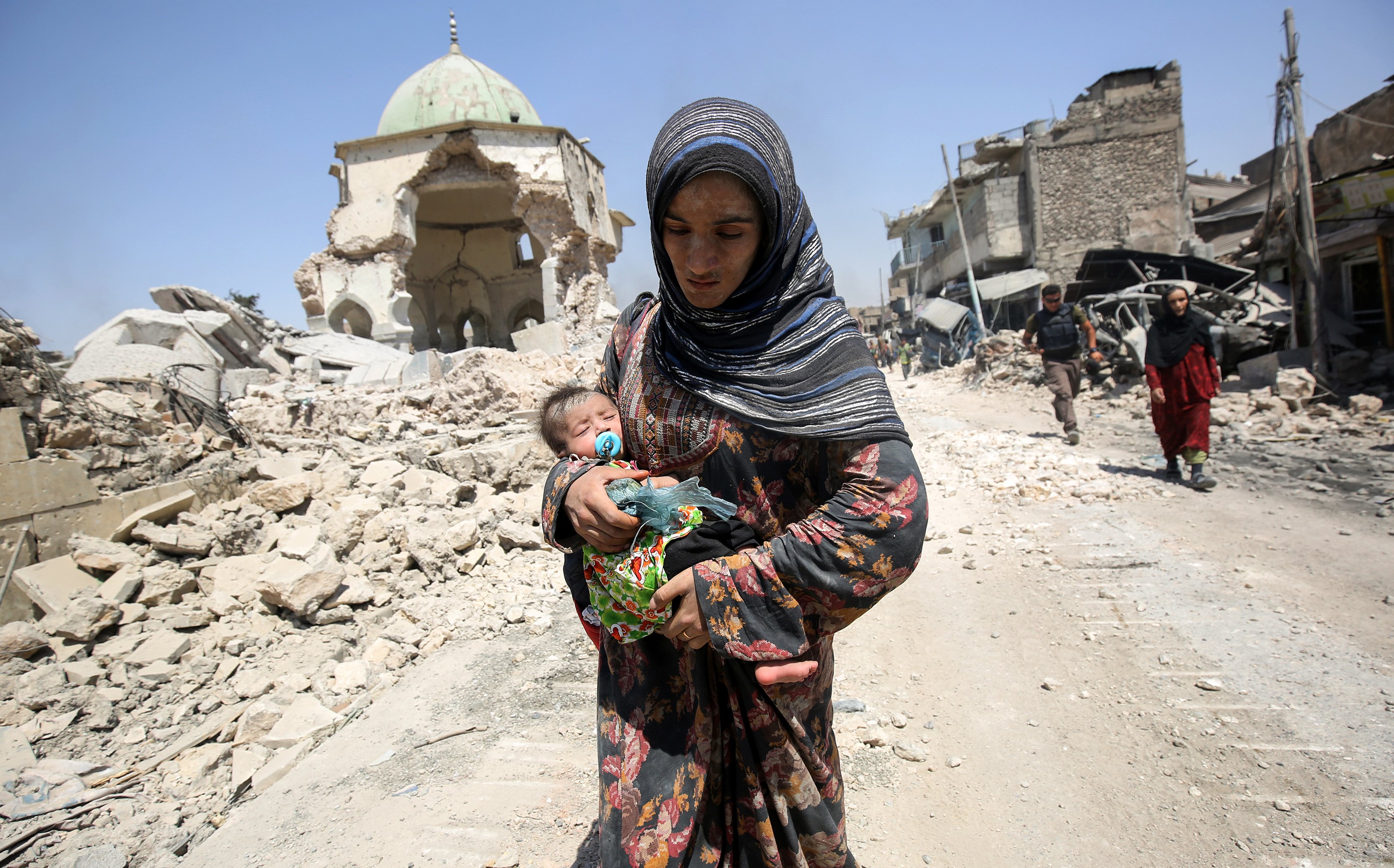 An Iraqi woman, carrying an infant, walks by the destroyed Al-Nuri Mosque as she flees from the Old City of Mosul on July 5, 2017, during the Iraqi government forces' offensive to retake the city from Islamic State (IS) group fighters..Iraqi forces have been closing in on the Old City in west Mosul for months, but the terrain combined with a la