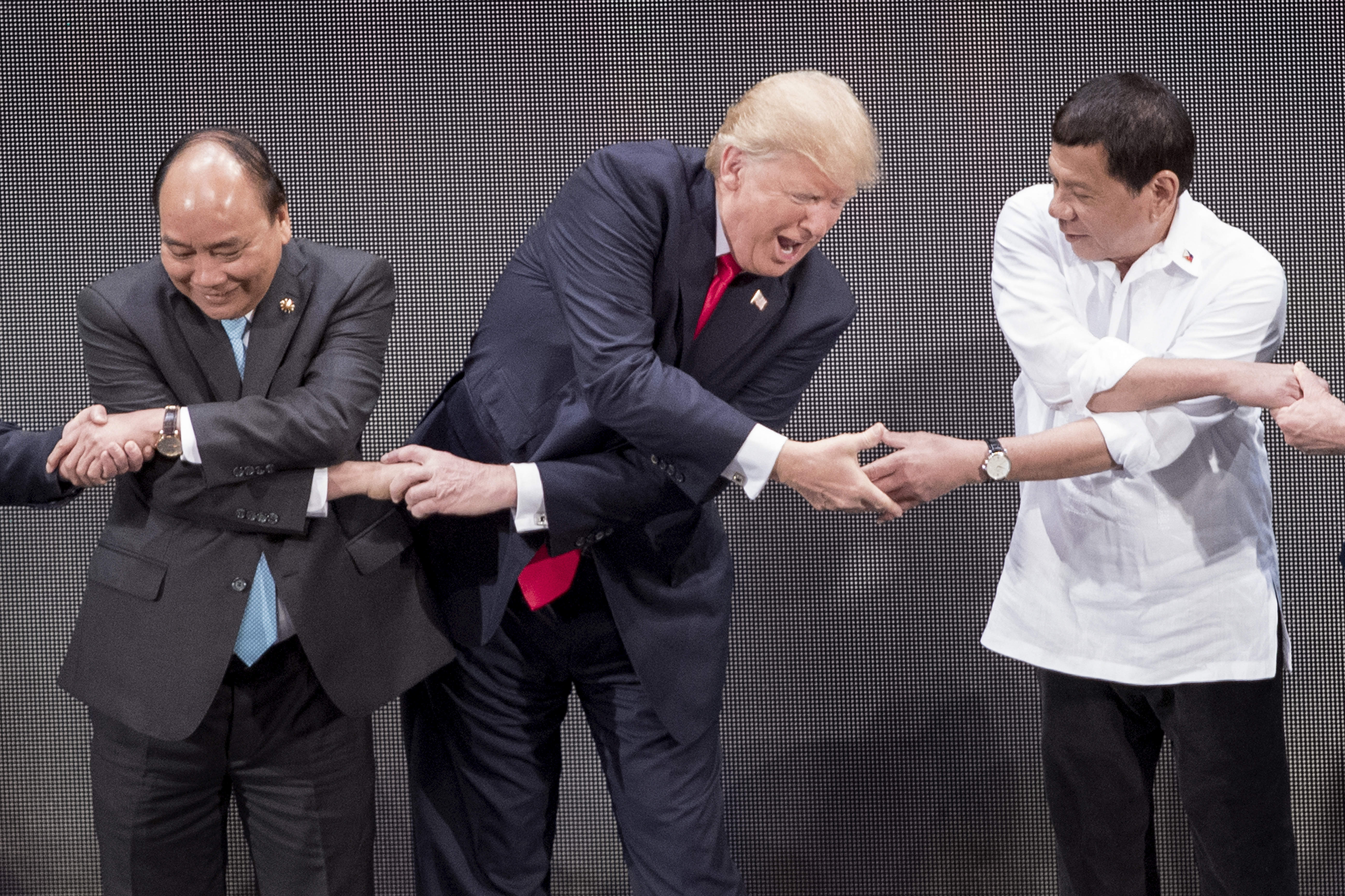 Vietnam's Prime Minister Nguyen Xuan Phuc (L), US President Donald Trump (C) and Philippine President Rodrigo Duterte join hands for the family photo during the 31st Association of South East Asian Nations (ASEAN) Summit in Manila on November 13, 2017. .World leaders are in the Philippines' capital for two days of summits.  / AFP PHOTO / JIM WATSON