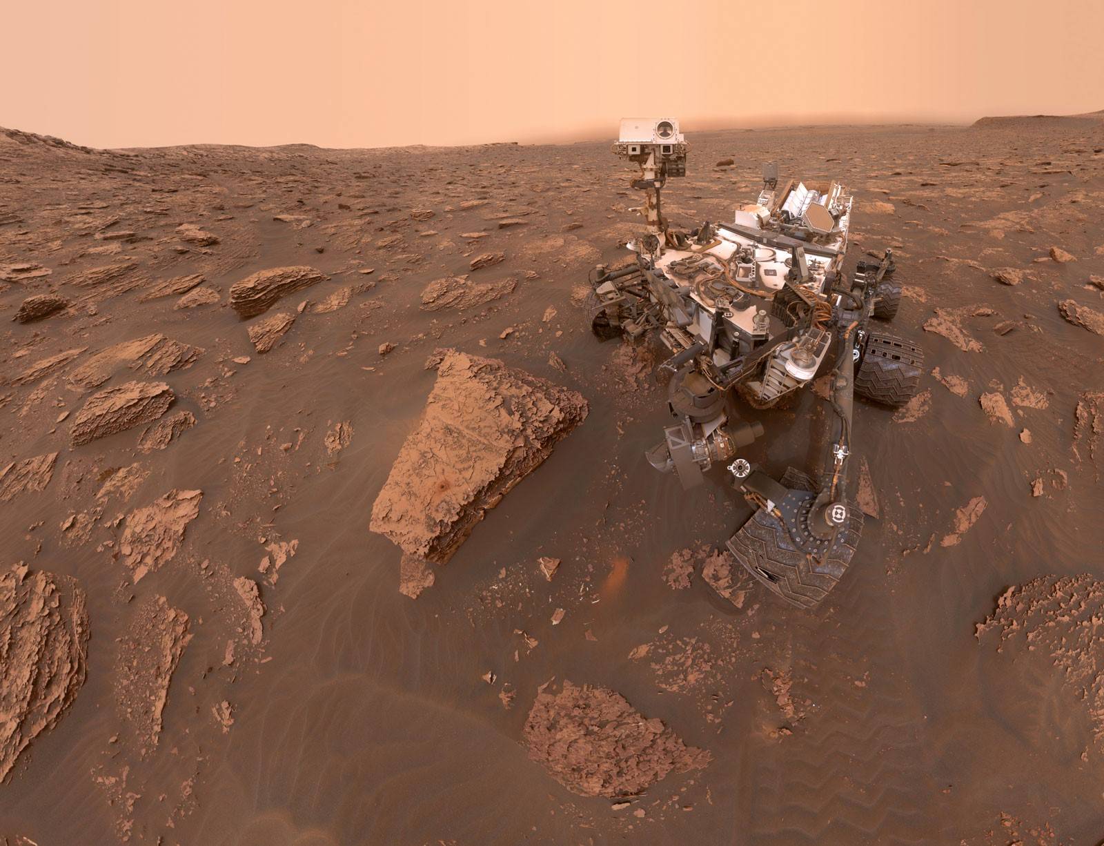 A Curiosity legutóbbi közzétett szelfije, a Duluth nevű mintavételi helyen, a Sharp-hegy alsó lejtőin. A Gale-kráter látási viszonyait jócskán megnehezítette, hogy a marsi vihar miatt sokkal kevesebb napfény jut a bolygó felszínére. (2018. június 20.)