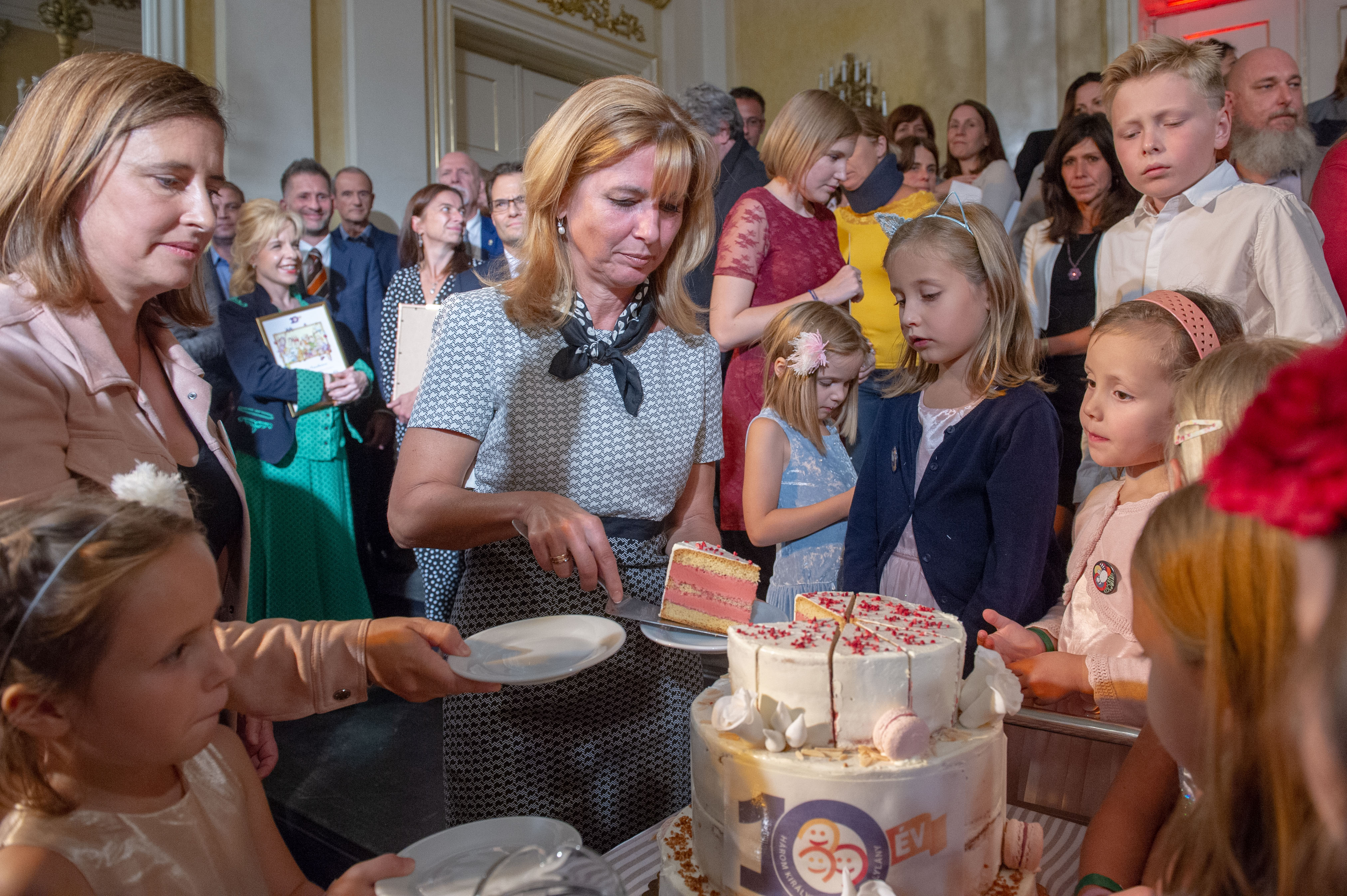 Herczegh Anita, a köztársasági elnök felesége tortát vág a Három Királyfi, Három Királylány Mozgalom ünnepségén. Balra Skrabski Fruzsina, a szervezet elnöke tartja a tányért.