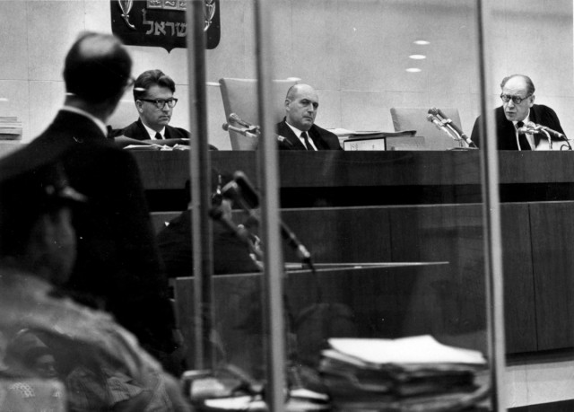 Szemközt az Eichmann-per bírái, bal oldalon állva a vádlott Adolf Eichmann, az üvegben tükröződve a közönség.
