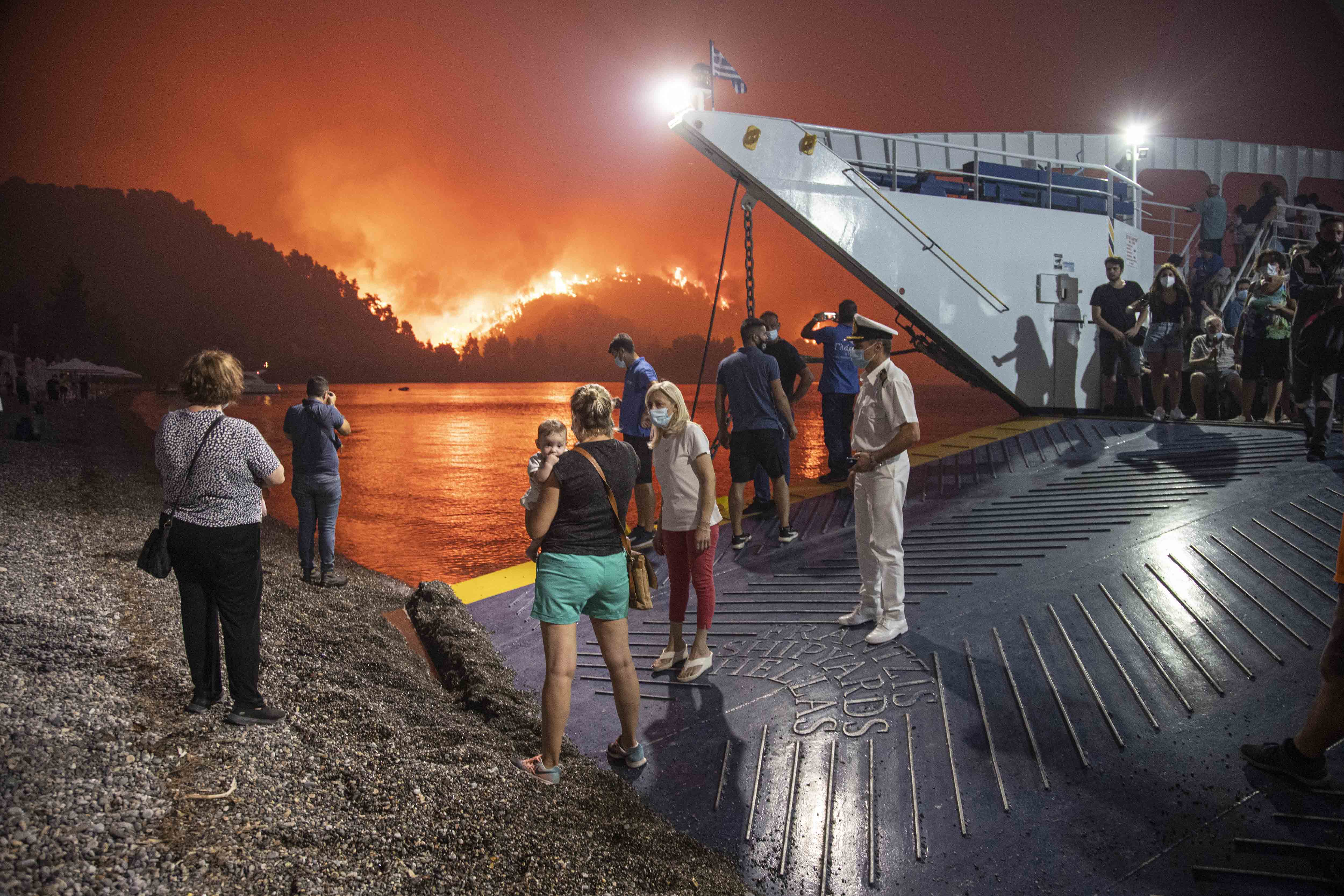 Miközben a lángok lassan elérik a görög Evián lévő, tengerparti Limni falut, az emberek kompon hagyják el a szigetet 2021. augusztus 6-án.