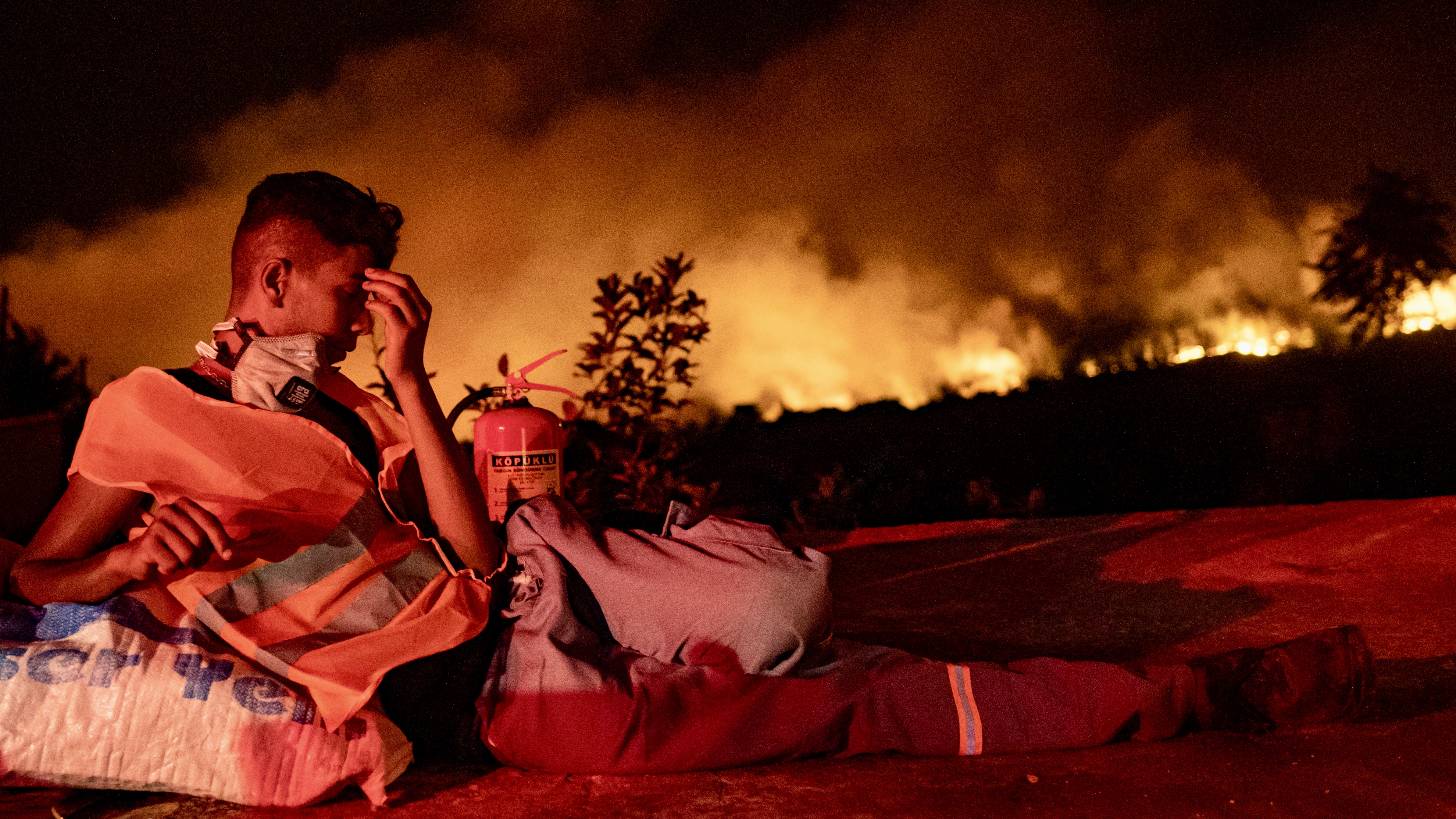 Önkéntes tűzoltó pihen a lángok mellett a törökországi Akcayaka közelében, 2021. augusztus 6-án.