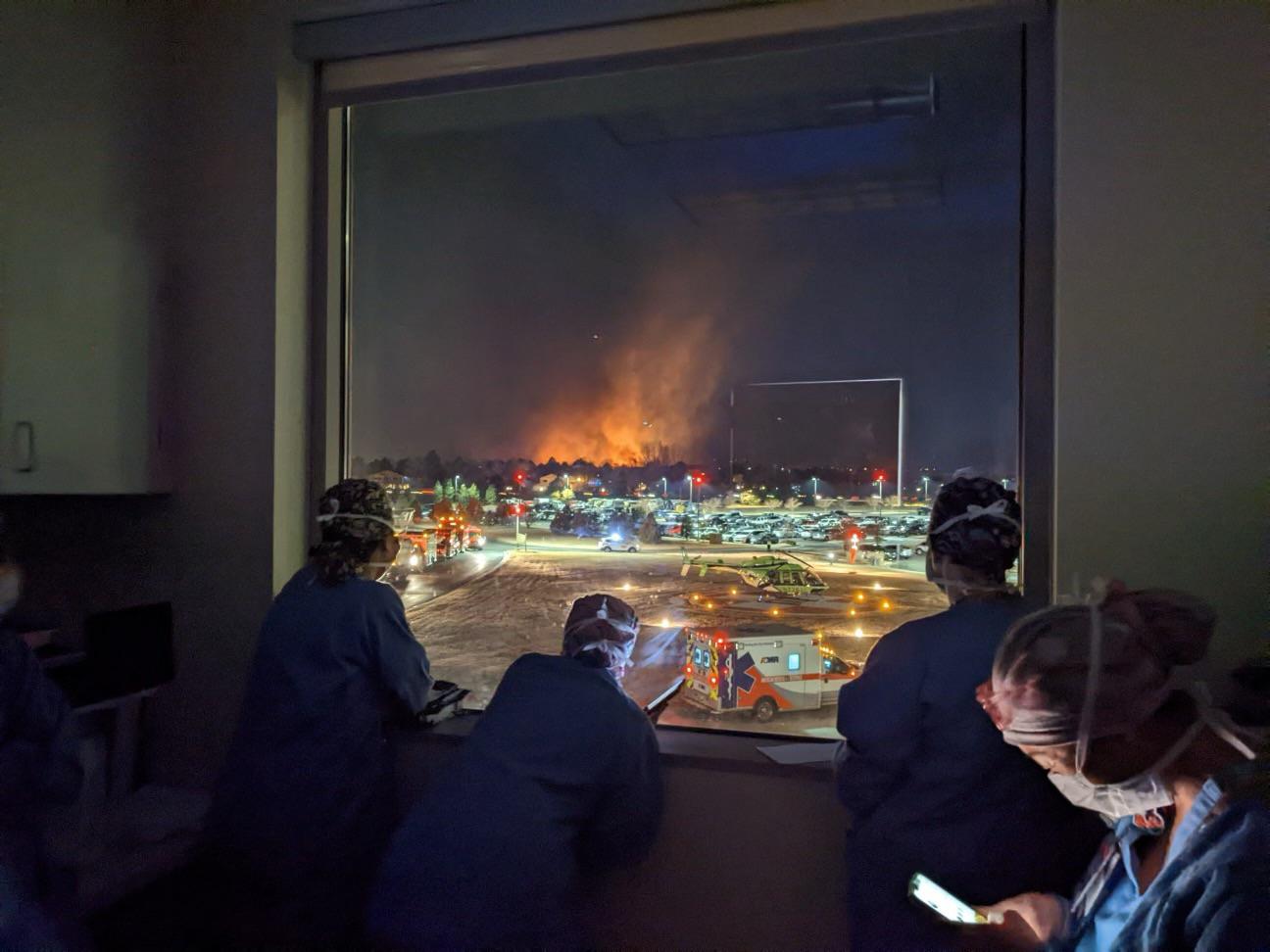 A 2020-as évek egyetlen fényképen: maszkos kórházi ápolók nézik a közelben tomboló tűzvészt