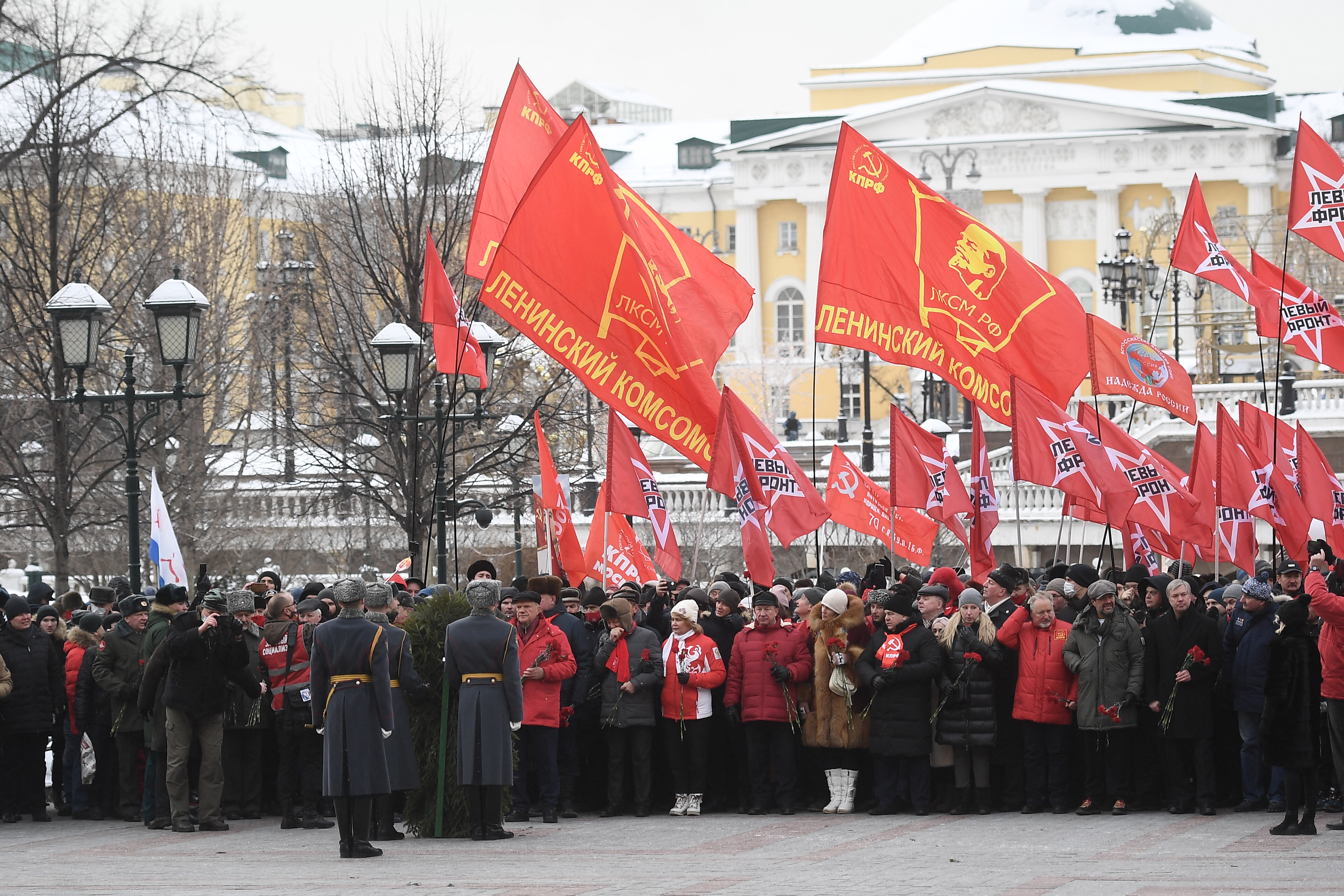 Lenin-portrés Komszomol-zászlókat lobogtatva koszorúznak az orosz kommunisták a Kremlnél 2021 februárjában