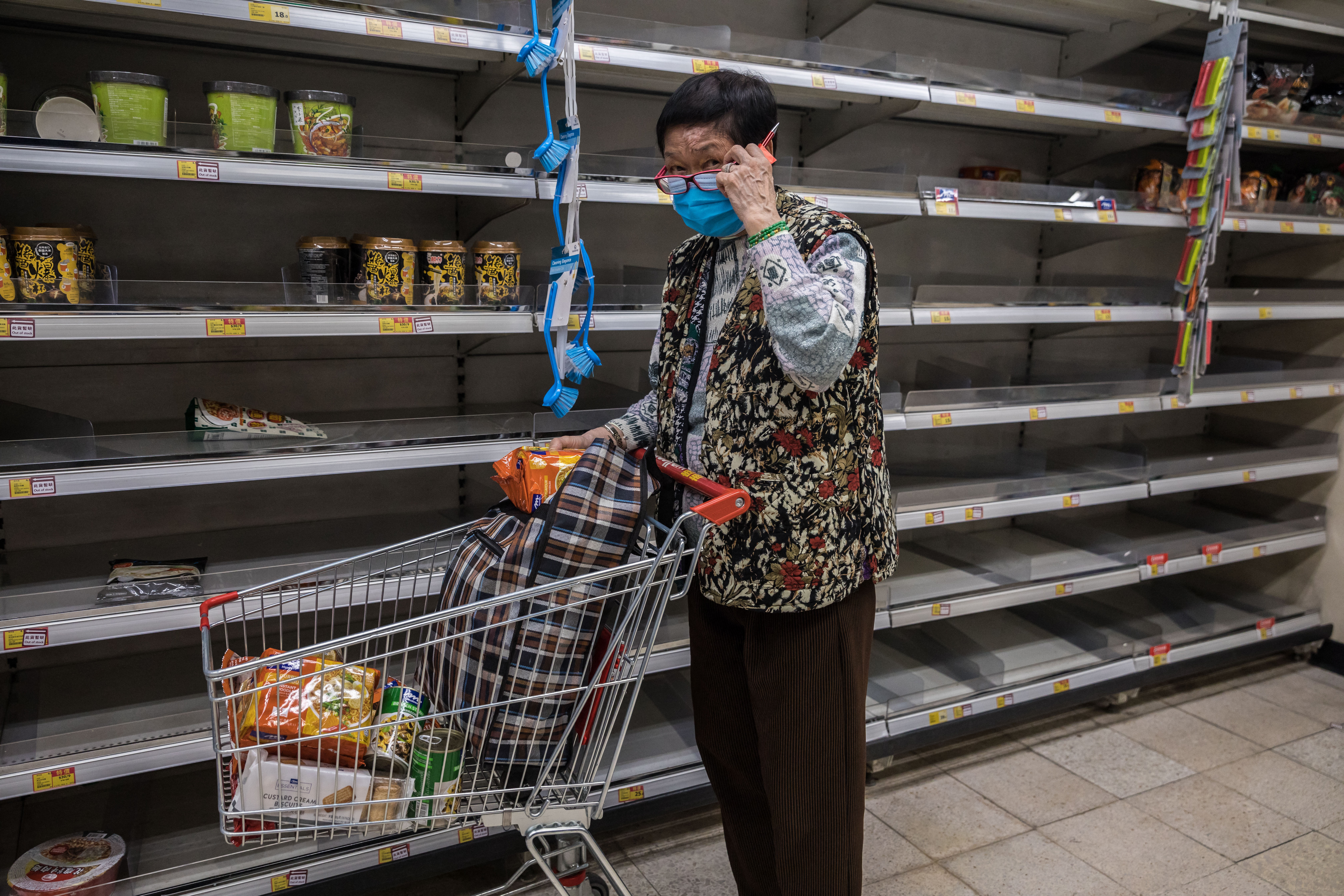 Nő vásárol egy hongkongi szupermarketben, kiürült polcok mellett.