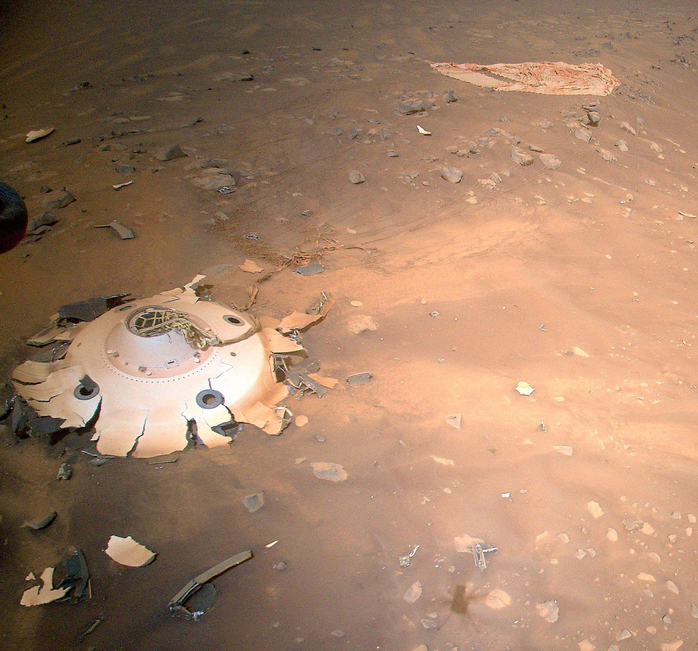 A Perseverancet és az Ingenuityt Marsra szállító kapszula hátuljának (bal lent) maradványai és a szuperszonikus ejtőernyő (jobb fent) a Mars-helikopter felvételén