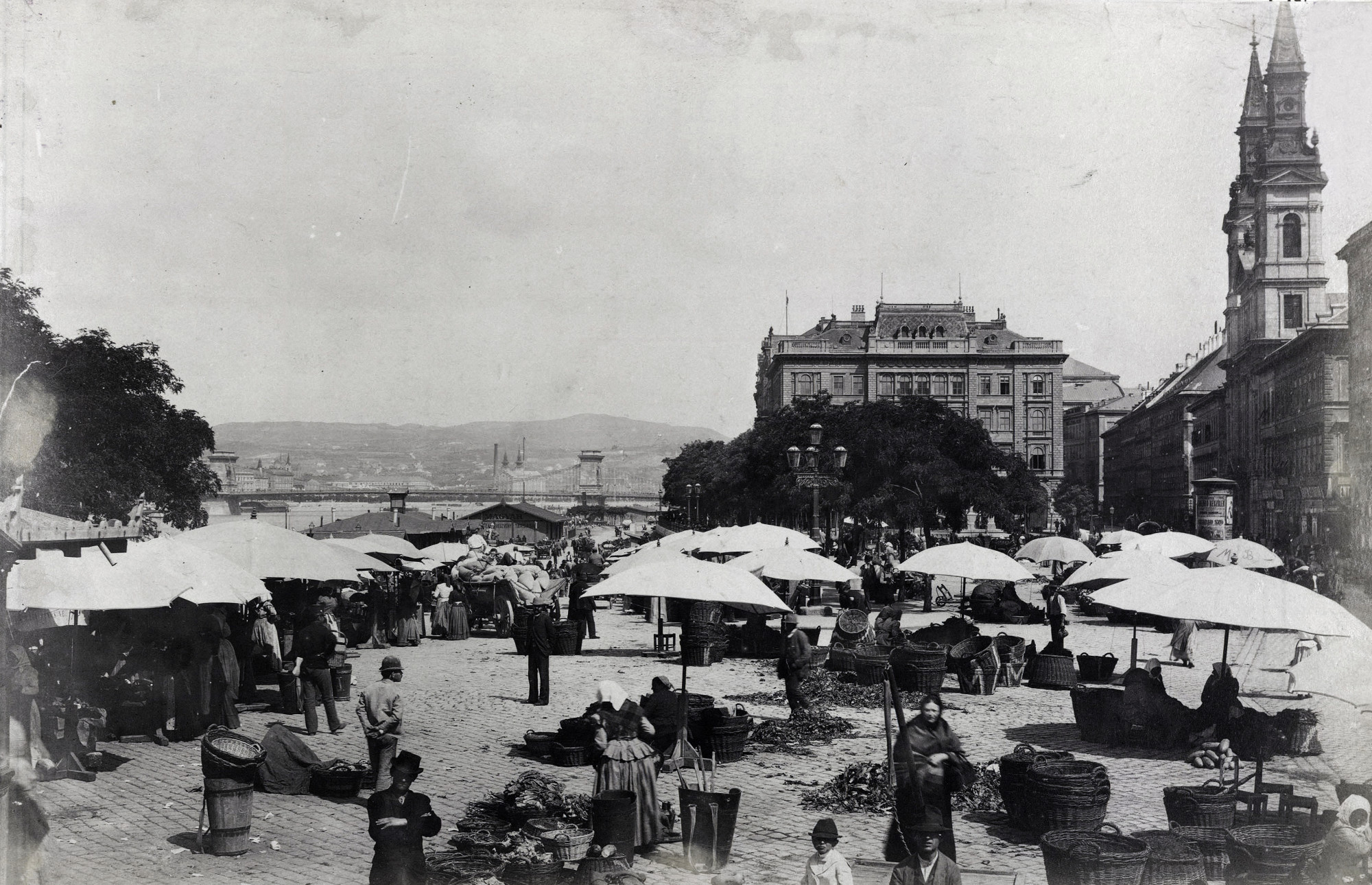 Piac a budapesti Petőfi téren 1874–1882 között. Balra a háttérben a Lánchíd, jobbra a Nagyboldogasszony ortodox székesegyház.