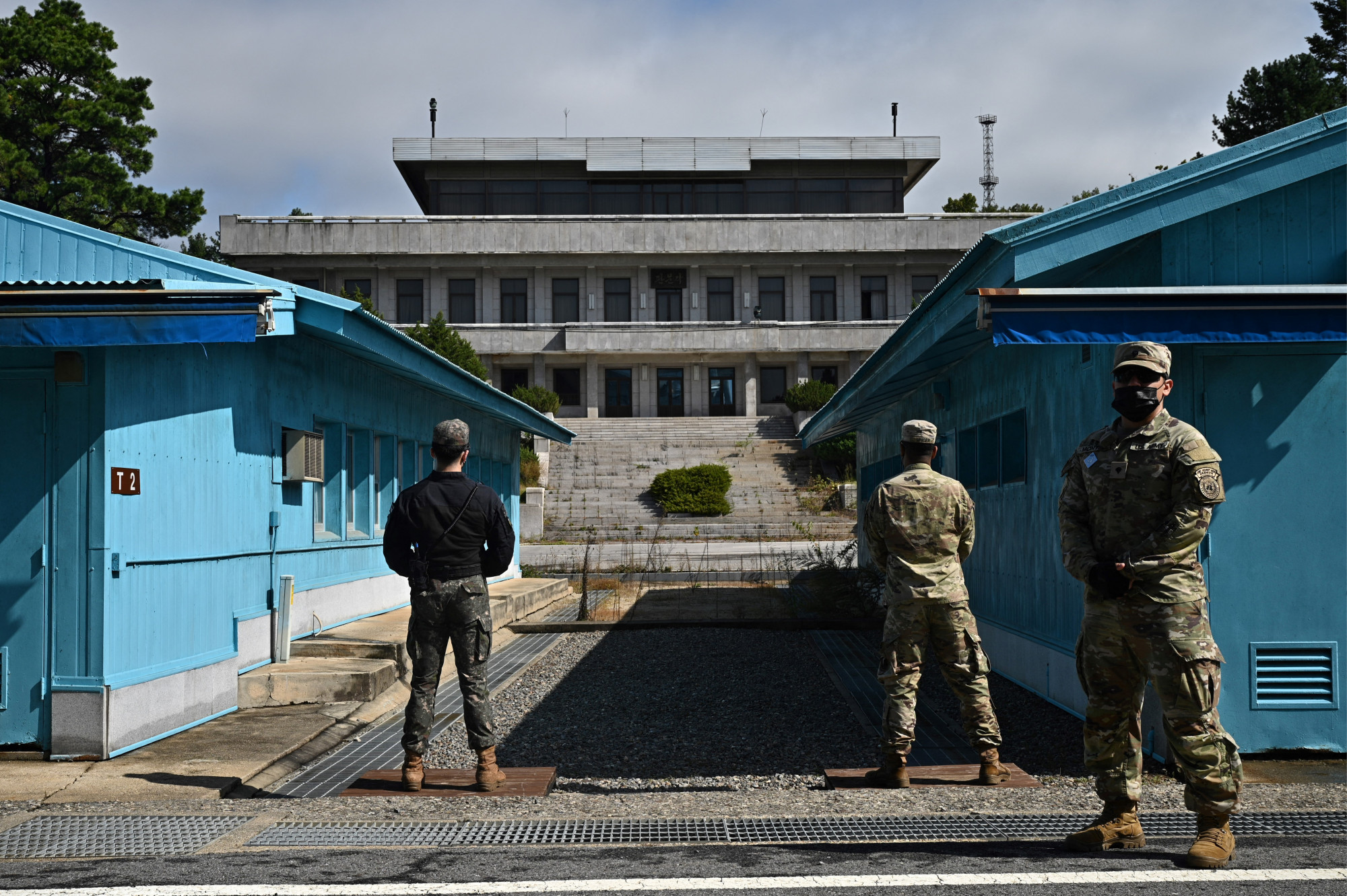 ENSZ-katonák (j) és egy dél-koreai katona (b) őrködnek Panmindzsonban a "tűzszüneti falu" észak-koreai oldalán álló Panmon Csarnok előtt.