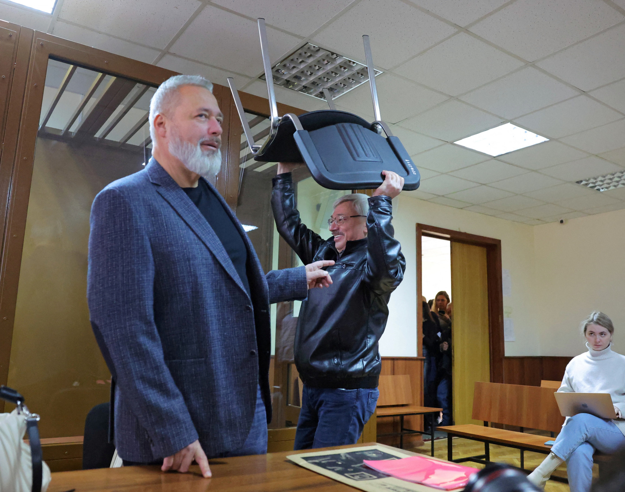 Oleg Orlov a saját székét cipeli, míg Dmitrij Muratov mosolyogva áll a bíróság előtt.