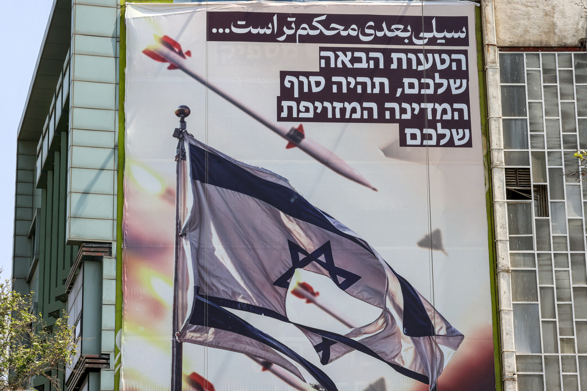 Óriás transzparens Teheránban április 14-én. Az izraeli zászló feletti perzsa felirat szerint: „a következő csapás keményebb lesz”, míg a héber nyelvű szöveg szerint „a következő hibátok a kamuállamotok végét jelenti”.