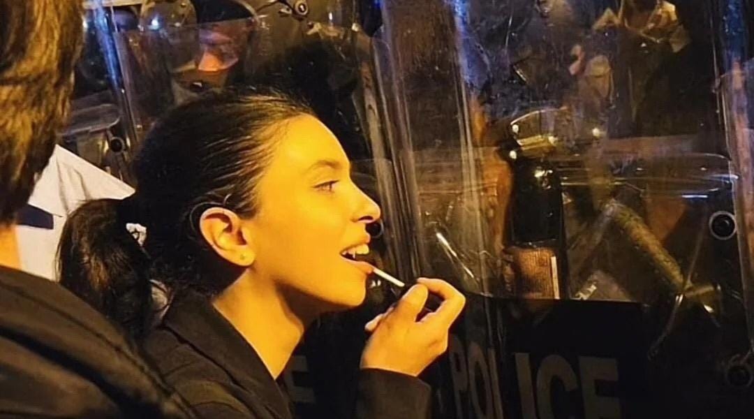 Tüntető a rendőri pajzs tükrében rúzsozza magát a külföldi ügynöktörvény elleni tüntetésen, 2024-ben. Nem fél.